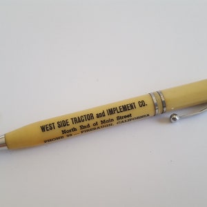 May include: A yellow plastic pen with a silver clip and a silver tip. The pen has the text "WEST SIDE TRACTOR and IMPLEMENT CO. North End of Main Street PHONE 58 FIRERAUGH, CALIFORNIA" printed on it.