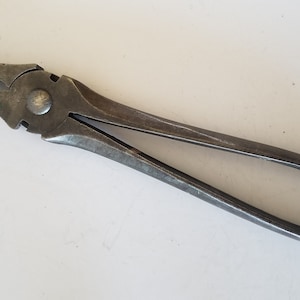 May include: A pair of vintage metal pliers with a silver finish. The pliers have a long handle and a slightly curved jaw.