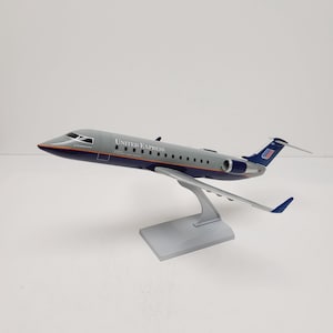 May include: A model airplane of a United Express jet. The plane is gray with a blue stripe and the words "United Express" printed on the side. The tail features the United Airlines logo. The model is mounted on a silver stand.
