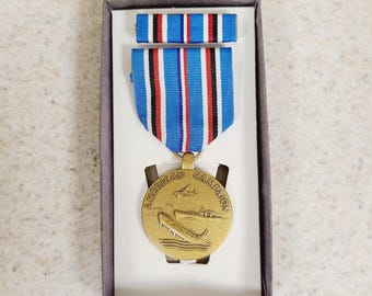 May include: A gold-colored American Campaign Medal with a blue, white, and red striped ribbon, presented in a box. The medal features an image of a ship and aircraft. The ribbon bar is also included.