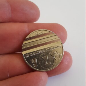 May include: A silver-colored metal token with the text "DISTRIBUTORE AUTOMATICI" and the letter "Z" in the center. The token also has a small image of a cup of coffee and a glass.