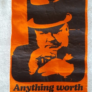 May include: Orange banner with a black illustration of a man in a hat holding a bird. The banner reads "Anything worth having is worth cheating for..." in black text. Copyright now! designs san francisco.