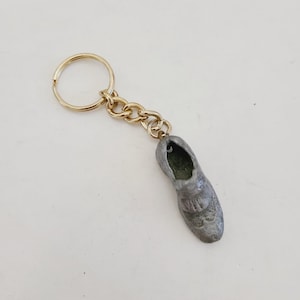 May include: A silver shoe charm attached to a gold key chain. The shoe charm is detailed and has a realistic look.