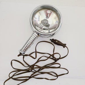 May include: A vintage chrome spotlight with a brown cord and a black plug. The spotlight has a round reflector and a long handle.