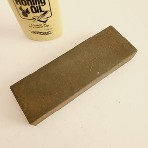 May include: A brown rectangular honing steel with a bottle of honing oil in the background. The bottle is labeled "Honing Oil" and "A Superior Oil for a Superior Edge".
