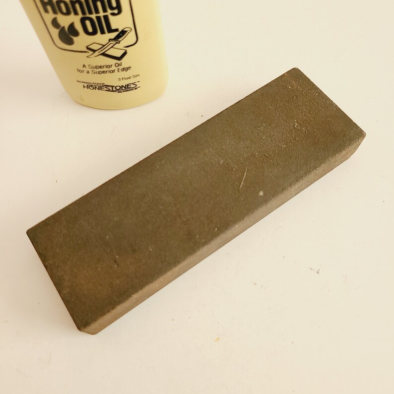 May include: A brown rectangular honing steel with a bottle of honing oil in the background. The bottle is labeled "Honing Oil" and "A Superior Oil for a Superior Edge".
