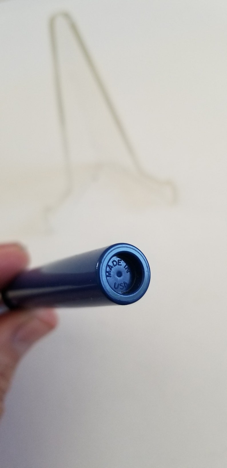 May include: Close-up of a navy blue pen with the text "MADE IN USA" on the end. The pen is cylindrical and appears to be made of plastic. A blurred object is in the background.