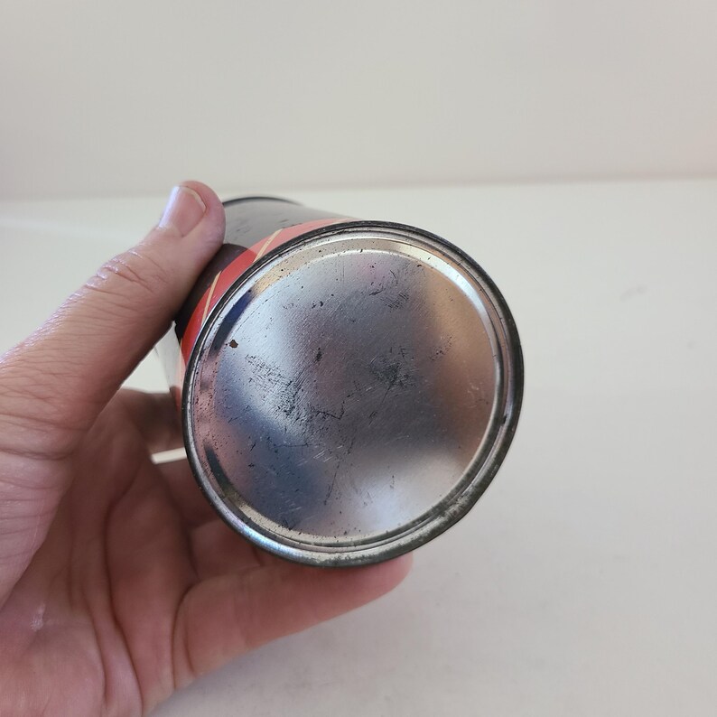 May include: The bottom of a silver metal can with a black and red label. The can is empty and has a smooth, shiny surface.