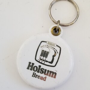 May include: White keychain with a round, white plastic charm featuring the words "Holsun Bread" and a black and white logo that says "Seal of Nutritional Value".