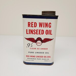 May include: A vintage can of Red Wing Linseed Oil, a clear amber pure linseed oil product. The can is white with red and blue accents and features a red wing logo with the text "Reg. U.S. Pat. Off.". The text "95 Clear as Amber" is printed on the can, along with the company name "Red Wing Linseed Oil Div. Pittsburgh Plate Glass Co.".