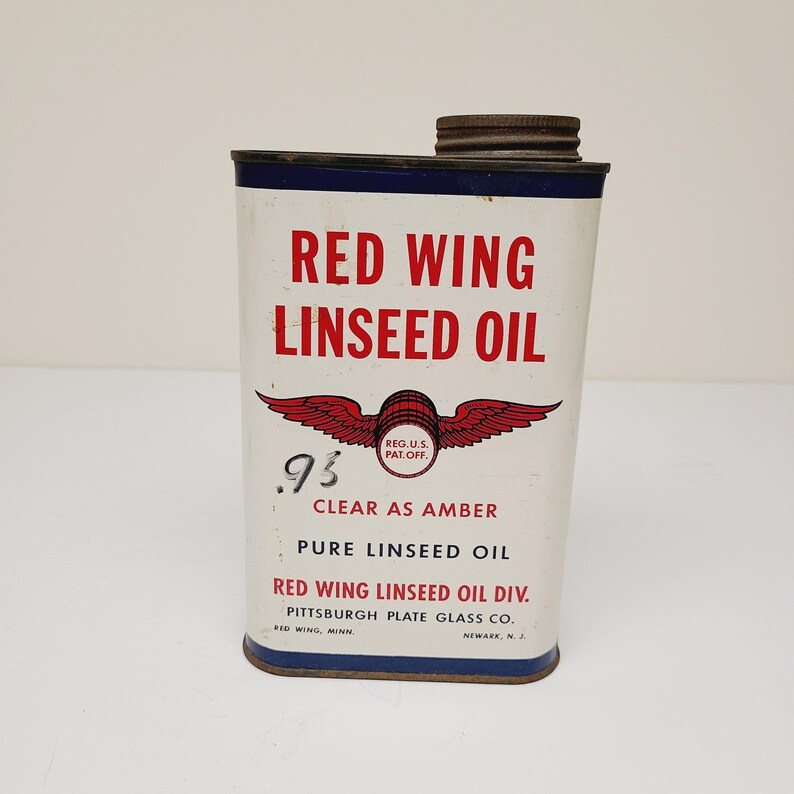 May include: A vintage can of Red Wing Linseed Oil, a clear amber pure linseed oil product. The can is white with red and blue accents and features a red wing logo with the text "Reg. U.S. Pat. Off.". The text "95 Clear as Amber" is printed on the can, along with the company name "Red Wing Linseed Oil Div. Pittsburgh Plate Glass Co.".