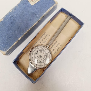 May include: Vintage Tacro Inc. map measurer in a blue box. The silver-toned instrument has a circular dial with numbers and a ribbed handle. The box contains a paper with text. Made in Germany.