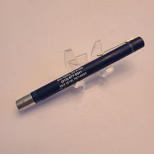 May include: A blue pen with a silver clip and gold accents. The pen has the text "Sun Valley, CA 91392 (213) 877-0341 FAX (818) 767-0453" printed on it.