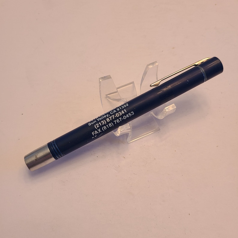 May include: A blue pen with a silver clip and gold accents. The pen has the text "Sun Valley, CA 91392 (213) 877-0341 FAX (818) 767-0453" printed on it.