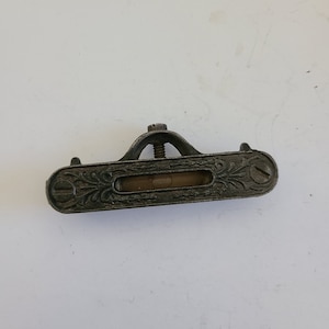 May include: A vintage cast iron level with an ornate design and a glass bubble level. The level is in good condition with some signs of wear.