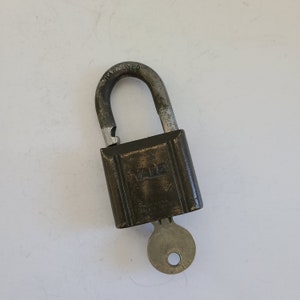 May include: A vintage Yale padlock with a hardened steel shackle and a brass body. The padlock has a keyhole and a key attached to it. The padlock is labeled "Yale" and "Hardened".