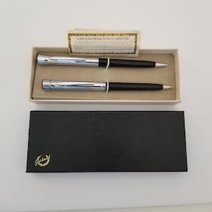 May include: A white box with a black lid containing two silver and black pens. The box has a gold sticker with the text "Garland Heirloom Guarantee" and a gold sticker with the text "Garland".