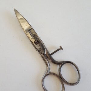 May include: Silver-toned metal scissors with a small screw on the handle. The scissors have the text "J.F. SEID U.S.A." on the handle.