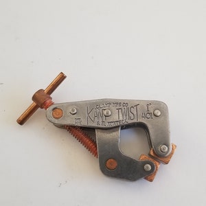 May include: A silver metal clamp with a copper-colored handle and a screw. The clamp is labeled "KAMP TWIST" and "CLAMP MFG CO. S. EL MONTE, CA. 401".