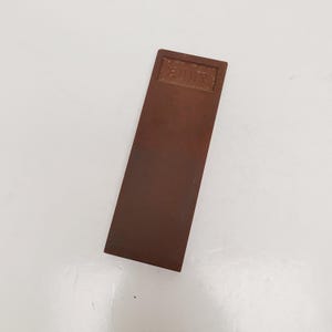 May include: A rectangular, brown sharpening stone with the word "ERIX" embossed at the top. The stone is a solid, uniform color and appears to be made of a dense material. The stone is designed for sharpening tools.