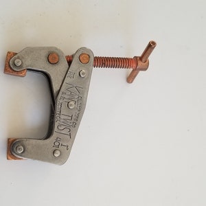 May include: A silver metal clamp with a copper-colored handle and a screw. The clamp is labeled "KAMP TWIST 1 40T" and "MADE IN USA".
