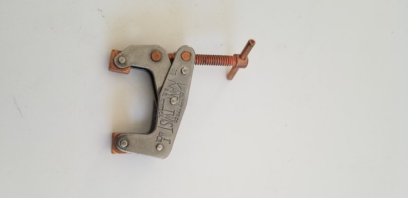 May include: A silver metal clamp with a copper-colored handle and a screw. The clamp is labeled "KAMP TWIST 1 40T" and "MADE IN USA".