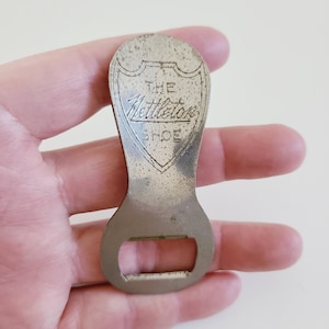 May include: Silver bottle opener with a shield-shaped design and the text "THE Nettleton SHOE" engraved on it.