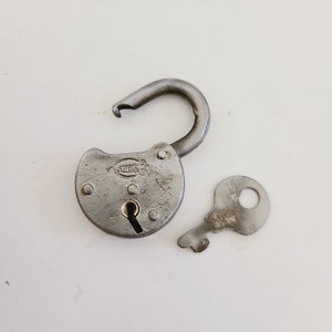 May include: An open, antique-style padlock with a matching key. The padlock is made of weathered metal, showing signs of age and use. The key is positioned next to the lock, suggesting it is ready to be used. The lock has the word "OHEIN" on it.