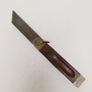 May include: A vintage sliding T-bevel tool featuring a dark brown wooden handle with a brass end cap and a brass locking nut. The tool has a long, flat, metallic blade that pivots from the handle, allowing for the measurement of various angles.