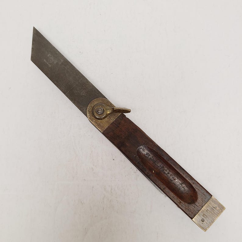 May include: A vintage sliding T-bevel tool featuring a dark brown wooden handle with a brass end cap and a brass locking nut. The tool has a long, flat, metallic blade that pivots from the handle, allowing for the measurement of various angles.