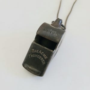 May include: A silver whistle with a black cord. The whistle has the text "THE ACME THUNDERER" engraved on the side.