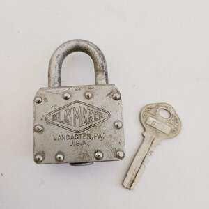 May include: A silver padlock with the text "SLAYMAKER LANCASTER, PA. U.S.A." and a matching silver key.
