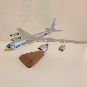 May include: A silver and white model airplane of a B-52 bomber on a wooden stand. The plane has the words "U.S. AIR FORCE" printed on the side.