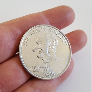 May include: A silver coin with a caricature of a man with a large nose and the text "The Great Society He Poorhouse Ruined Em 1984".