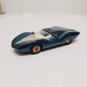 May include: A vintage die-cast toy car in a metallic teal blue finish. The car features a streamlined design with a silver accent on the hood and gold-colored wheels with red centers. The toy car is a collectible item.