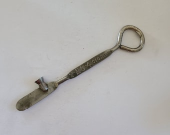 May include: A silver metal bottle opener with a small, round, metal cap opener on one end and a loop on the other end. The bottle opener is engraved with the text "7 26 4 CIGAR".