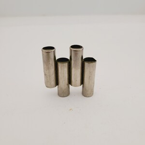 May include: A set of four silver-colored metal pipes, arranged in a staggered pattern, resembling a musical instrument.