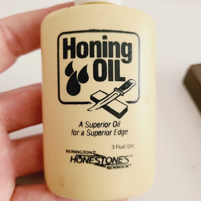 May include: A small, yellow plastic bottle of honing oil with a black label that reads "Honing Oil" and features a knife being sharpened on a honing stone. The label also says "A Superior Oil for a Superior Edge" and "Remington Honestones Remrock".