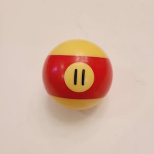May include: A yellow and red billiard ball with the number "11" printed in black on the center of the ball.