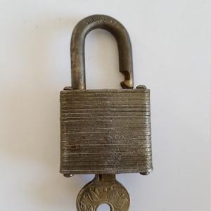 May include: A silver padlock with a keyhole and a brass key with a lion design. The padlock has a textured surface and is closed.