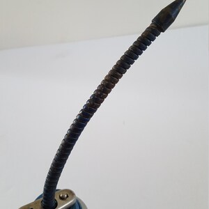 Puede incluir: Una lata de aceite plateada con una tapa azul y un largo pico de metal flexible. El pico est&aacute; doblado y tiene un ligero color &oacute;xido.