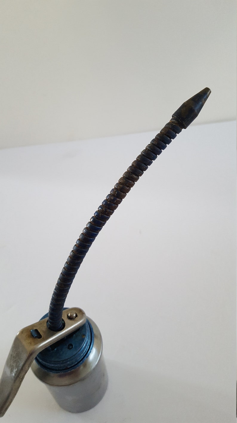 Puede incluir: Una lata de aceite plateada con una tapa azul y un largo pico de metal flexible. El pico est&aacute; doblado y tiene un ligero color &oacute;xido.