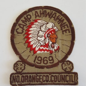 May include: A brown and tan embroidered patch with the text "Camp Ahwahnee 1969" and "No Orange Co. Council". The patch features a Native American chief wearing a headdress.