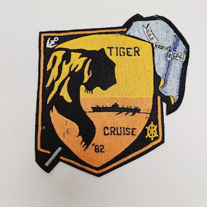 May include: Embroidered patch with a shield shape, featuring a tiger head silhouette in black and yellow. The text "TIGER CRUISE '82" is visible. A smaller patch with "U.S.S. RANGE (CV-61)" is attached.