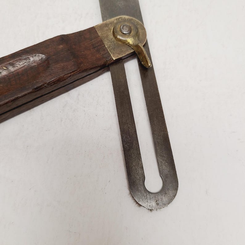 May include: A vintage sliding T-bevel tool featuring a dark brown wooden handle and a metallic blade. The two components are connected by a brass locking nut and a pivot mechanism, allowing the blade to be adjusted and secured at various angles.