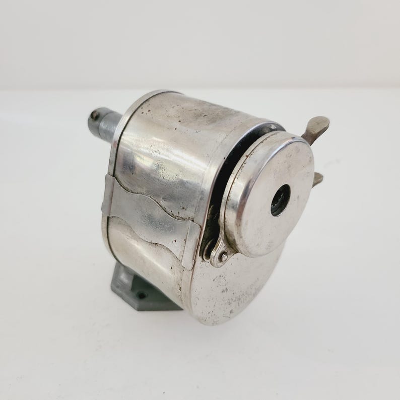Puede incluir: Un sacapuntas vintage de plata con manivela y base de metal. El sacapuntas tiene una abertura redonda para l&aacute;pices y una cuchilla de metal.