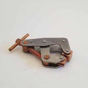 May include: A silver metal clamp with a copper handle and a screw. The clamp is labeled "K&W Twist 1" and "K&W 1" on the side.