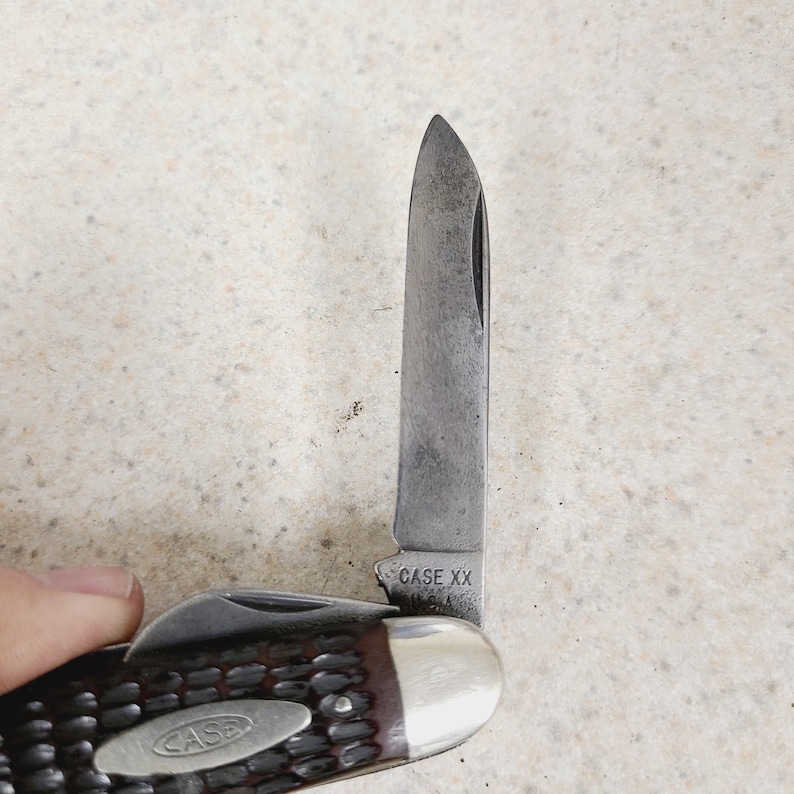 以下が含まれることがあります： 銀色の刃と茶色の柄が付いた、部分的に開いたポケットナイフ。 刃には「CASE XX」のマークがあります。 ハンドルにはテクスチャパターンとシルバーのエンドキャップが付いています。 ナイフは手で持たれています。