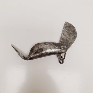 May include: An antique, metal tool with a curved blade and a pointed end. The tool has a hinged, semi-circular blade and a small ring attached to the body. The metal has a worn, aged appearance.