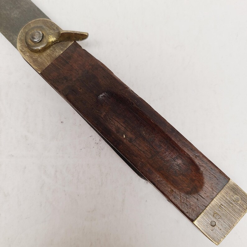 May include: A sliding T-bevel tool featuring a dark brown wooden handle with a recessed center groove. The tool includes a brass locking nut and a brass end cap. The metal blade is partially visible, extending from the brass pivot mechanism.